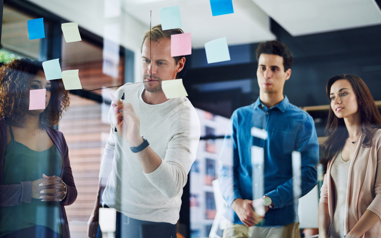 Businessman, coach and writing with team in meeting on glass board for presentation, brainstorming or planning. Male person, group or employees with schedule tasks for project management at workplace.